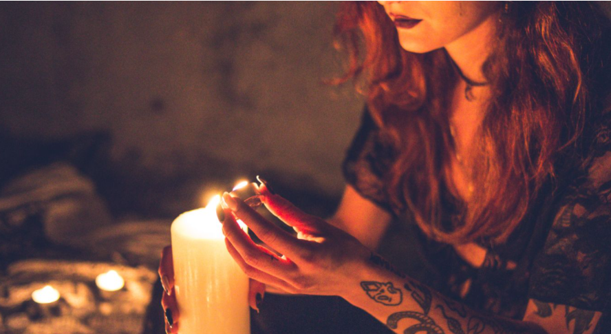 a witchy looking woman with tattoos in a circle with a candle