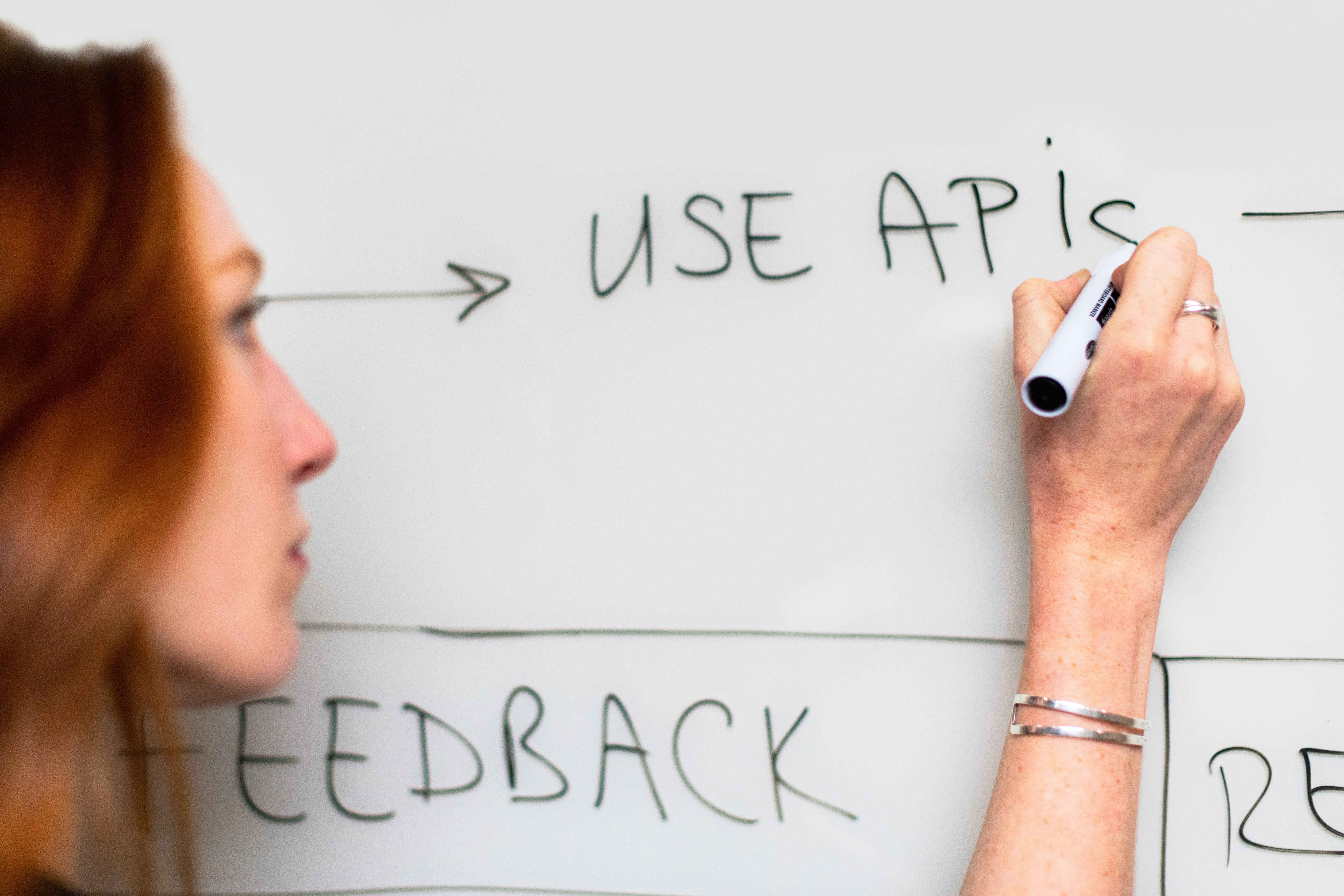 A really good image of a red haired woman writing "use APIs" on a whiteboard